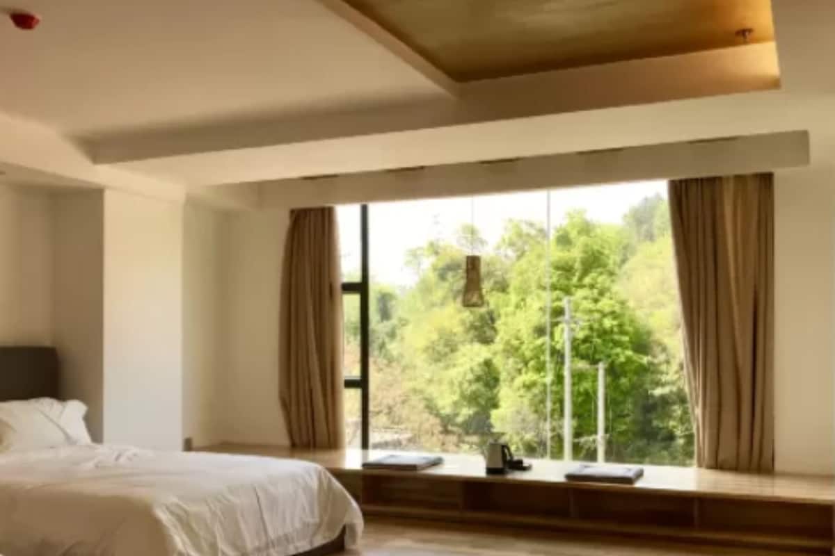 A bedroom with a large window, a bed, and a bedside table.