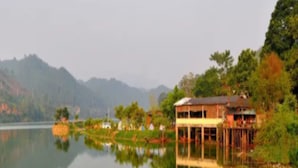 A lakeside property with a large building, reflecting in calm water, surrounded by greenery and hills. - Qing Gu Ju (Zhaoqing)