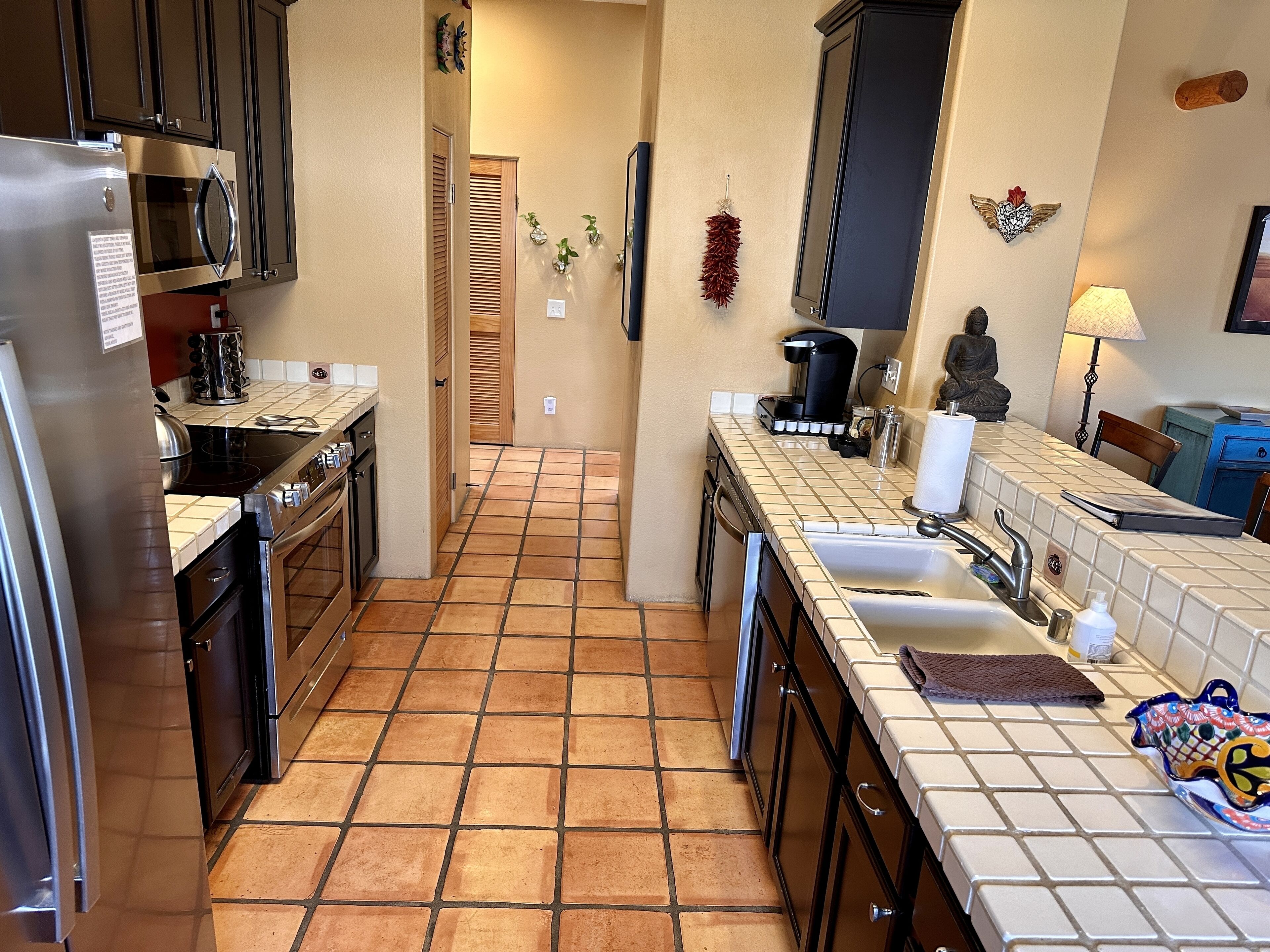 A compact kitchen with a refrigerator, stove, microwave, and sink. There are decorative items on the walls and a small statue.