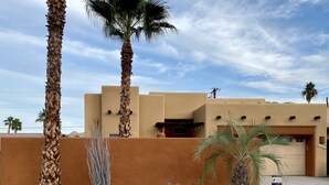A desert-style building with a stucco exterior, palm trees, and a rock garden. - Serene Desert Escape-Salt Water Pool & Jacuzzi/Fire Pit/Views #067047 3bd (La Quinta)