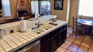 A kitchen with a tiled backsplash, a built-in dishwasher, a sink, and a window with blinds. - Serene Desert Escape-Salt Water Pool & Jacuzzi/Fire Pit/Views #067047 3bd (La Quinta)