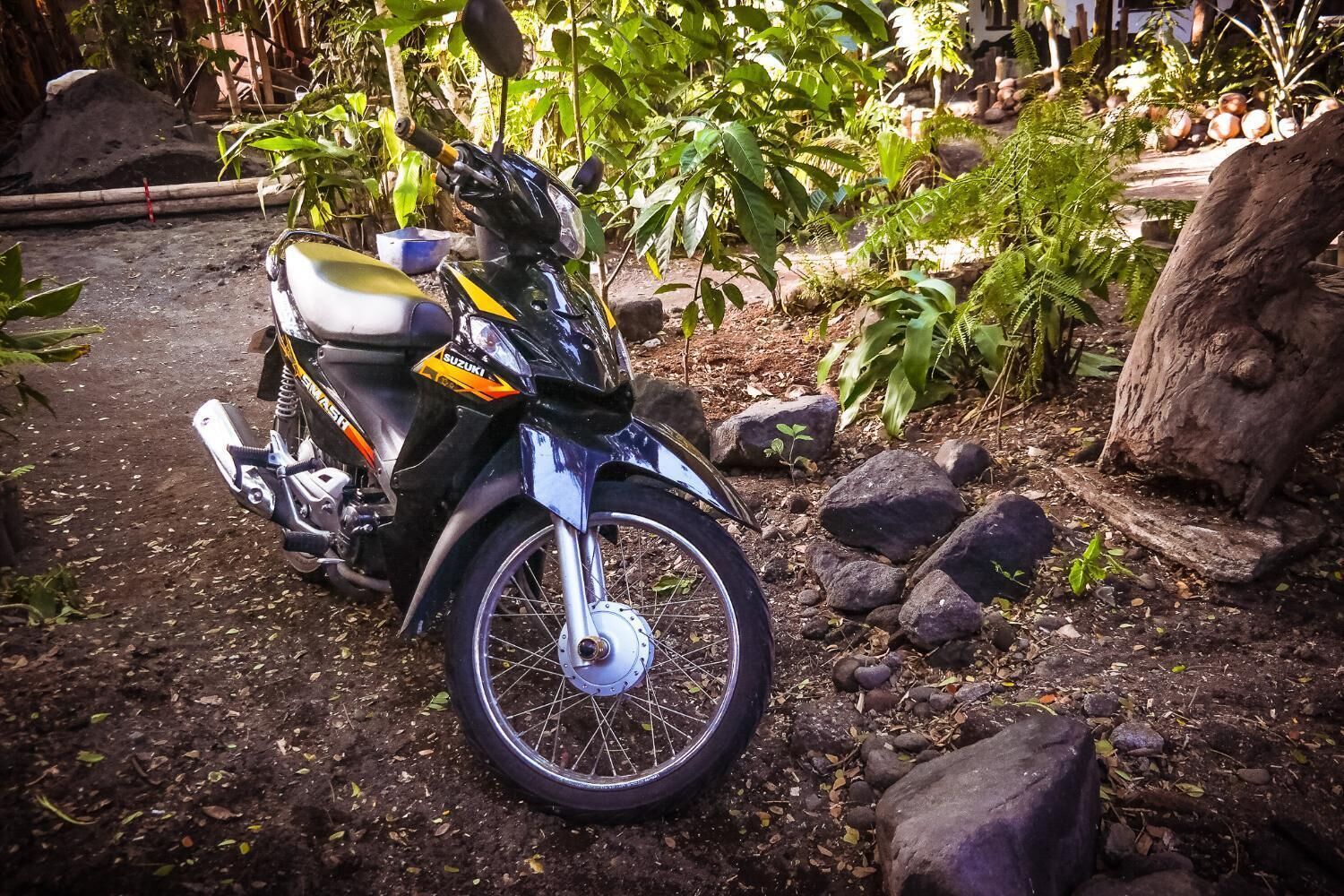 Una motocicleta negra estacionada en un camino de tierra rodeada de rocas y follaje.