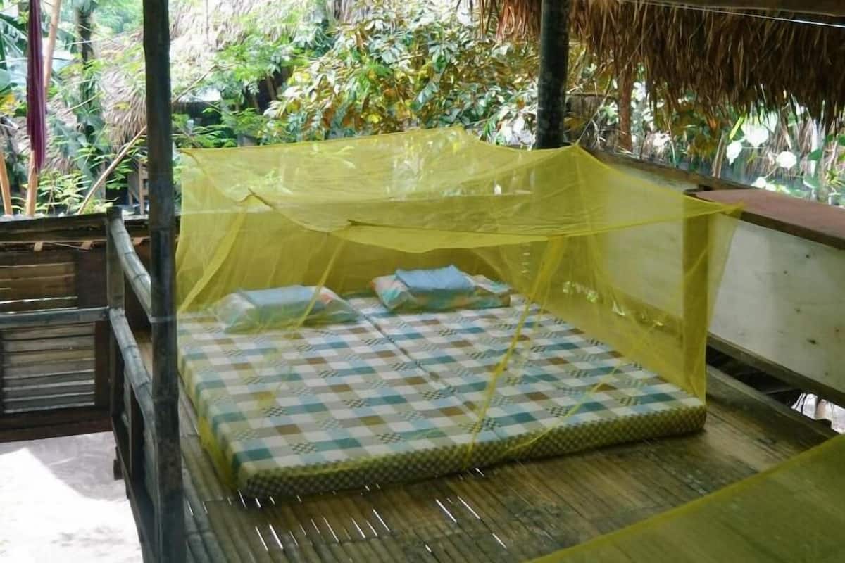 A single bed with a mosquito net in a rustic hut with a thatched roof.