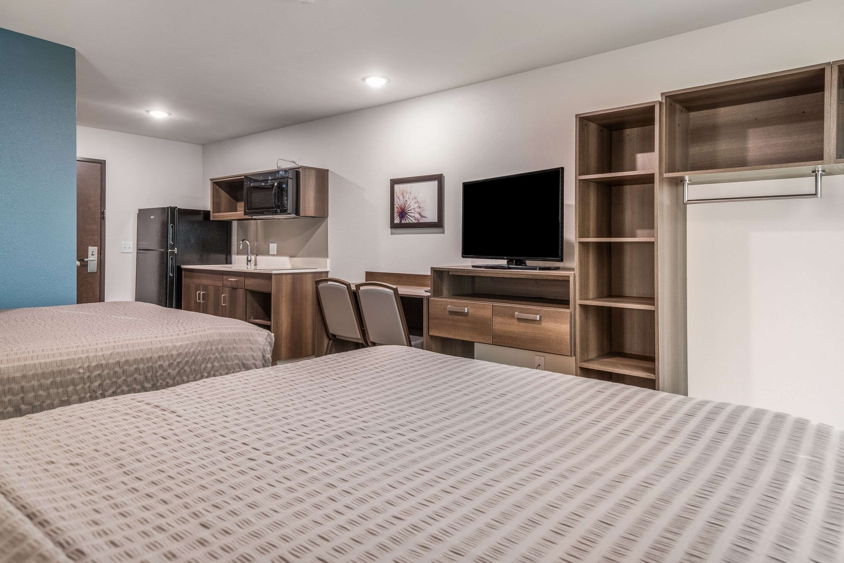 A hotel room with two beds, a kitchenette, a TV, and built-in shelves.