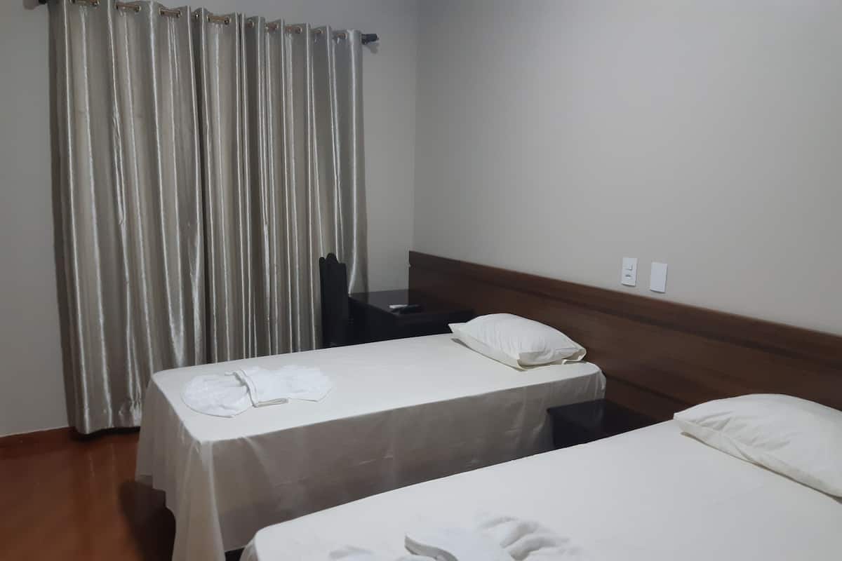 A hotel room with two single beds, a wooden headboard, a small table, and a curtain.