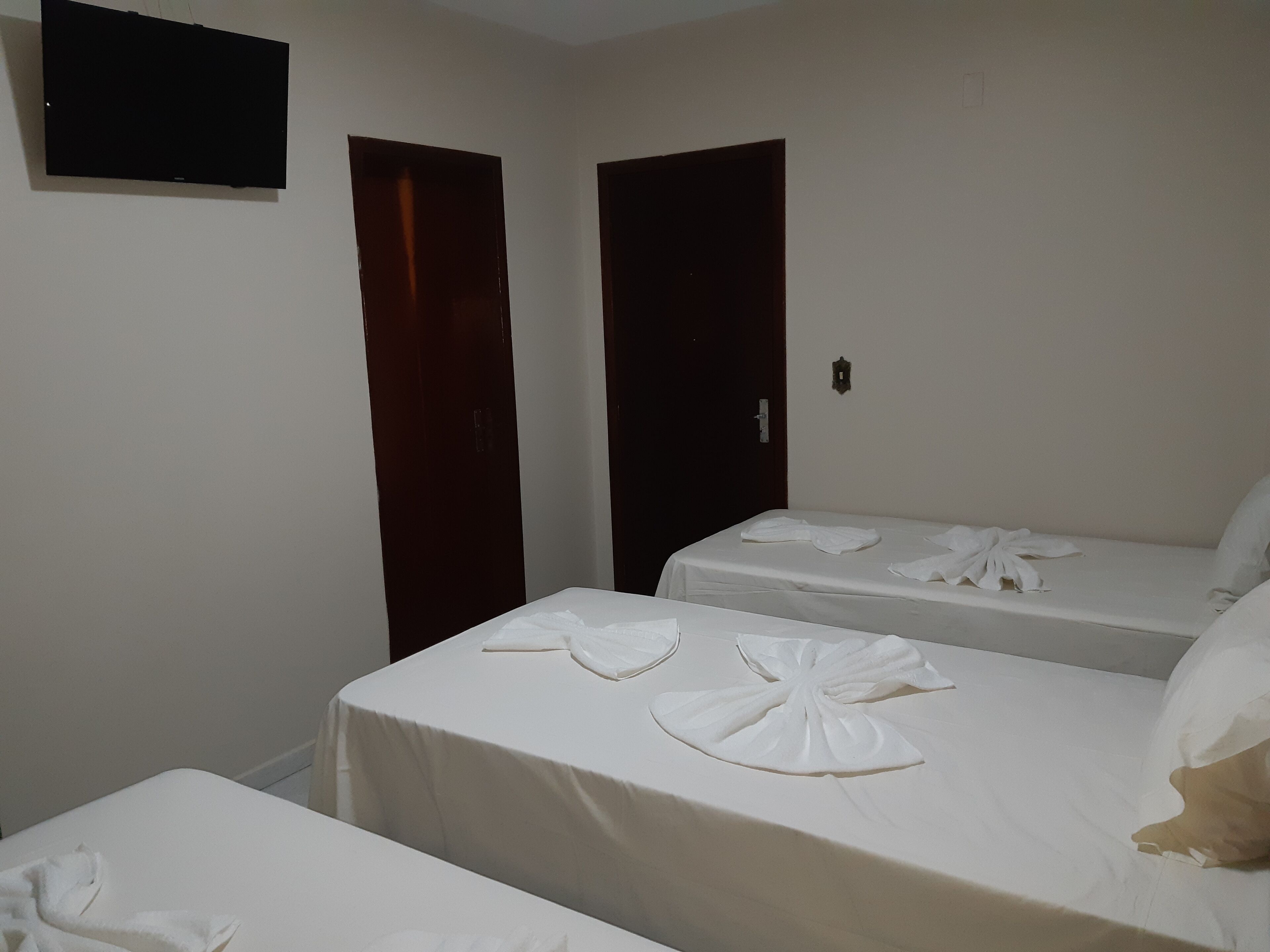 Ein Hotelzimmer mit zwei Einzelbetten, einem an der Wand befestigten Flachbildfernseher und zwei Türen.