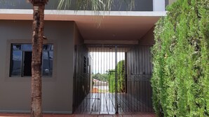 Un edificio moderno con entrada protegida, una palmera y un seto bien cuidado.