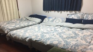A room with two beds, each with patterned bedding and pillows, a green ottoman, and a window with curtains. - ASHITOMI HOUSE (南城市)