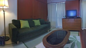 A living room with a sofa, a television, a lamp, and a wicker chair. - ASHITOMI HOUSE (南城市)