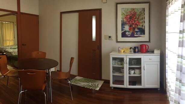 A room with a dining table and chairs, a white cabinet with kitchenware, a painting on the wall, and a door leading to another room. - ASHITOMI HOUSE (南城市)
