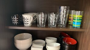 A shelf with various kitchenware including mugs, glasses, and bowls. - ASHITOMI HOUSE (南城市)