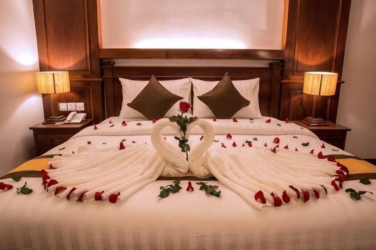 Una camera d'albergo con un letto, due comodini, una testiera in legno e una TV a muro.