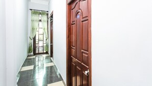 A hallway with a checkered floor, a wooden door with a sign, and green curtains.