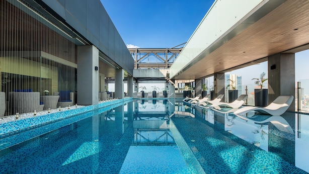 A modern indoor swimming pool with clear blue water, lounge chairs, and a view of the city skyline. - Yangon Thanlwin Hotel (Yangon)