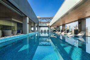 A modern indoor swimming pool with clear blue water, lounge chairs, and a view of the city skyline. - Yangon Thanlwin Hotel (Yangon)