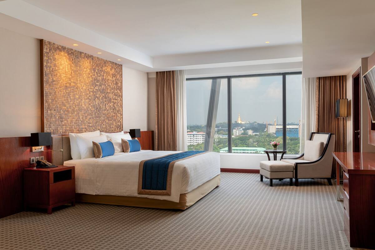 A hotel room with a large bed, a desk, a chair, and a view of a cityscape.