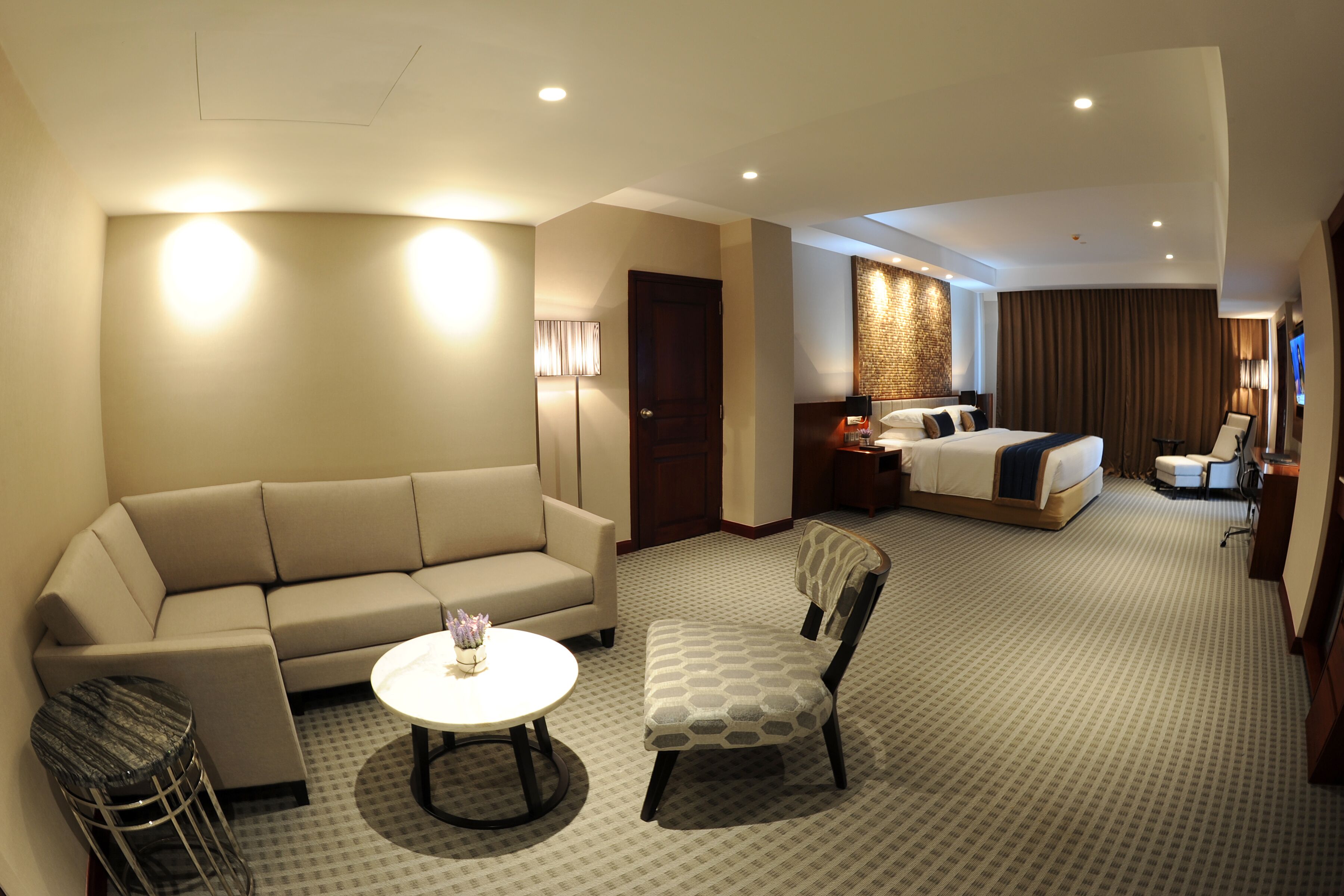 Une chambre d’hôtel avec un canapé, une petite table ronde, un fauteuil à motifs, un lit, une table de chevet, une lampe et un téléviseur.