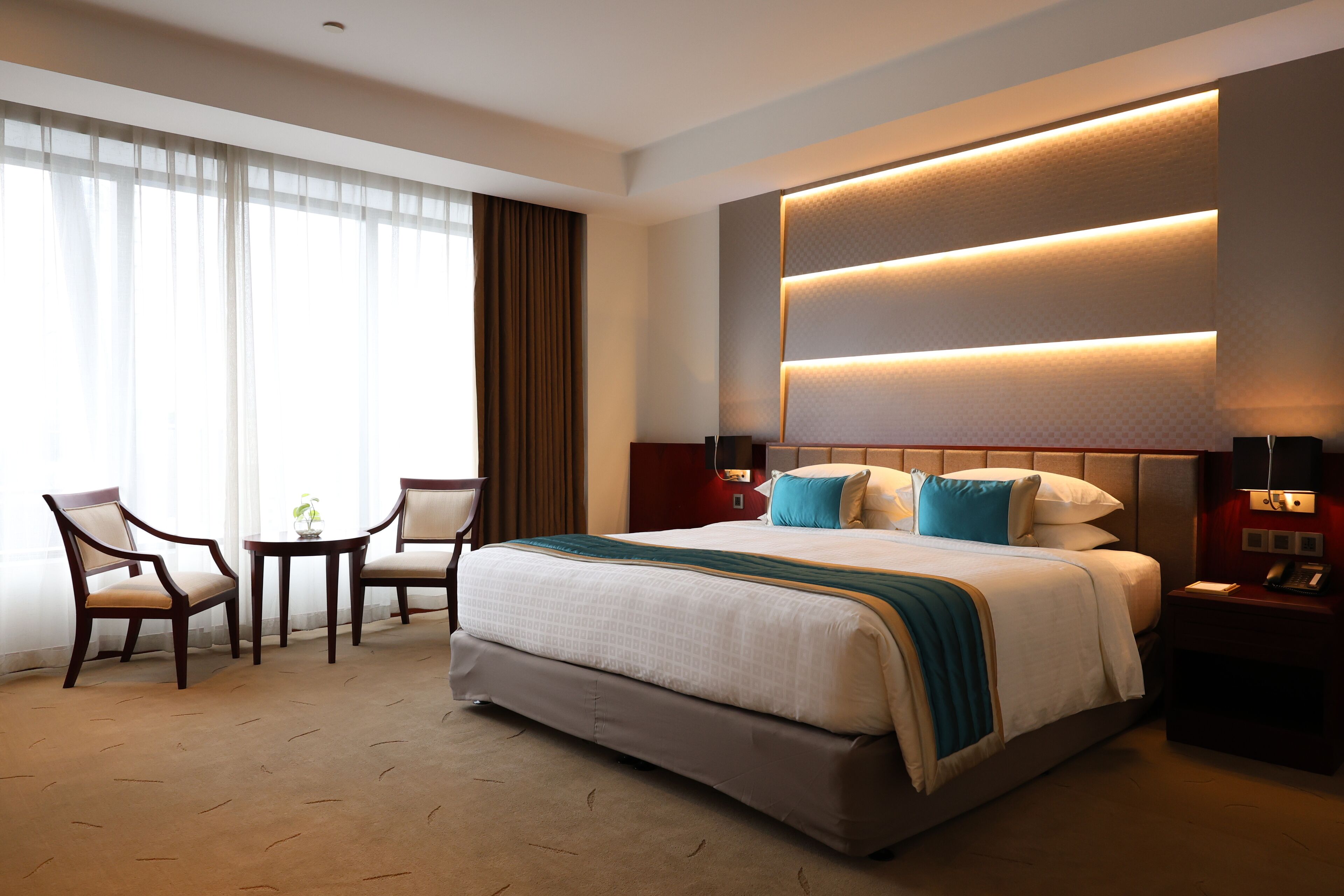 A hotel room with a large bed, two chairs, a small table, and a nightstand with a phone.