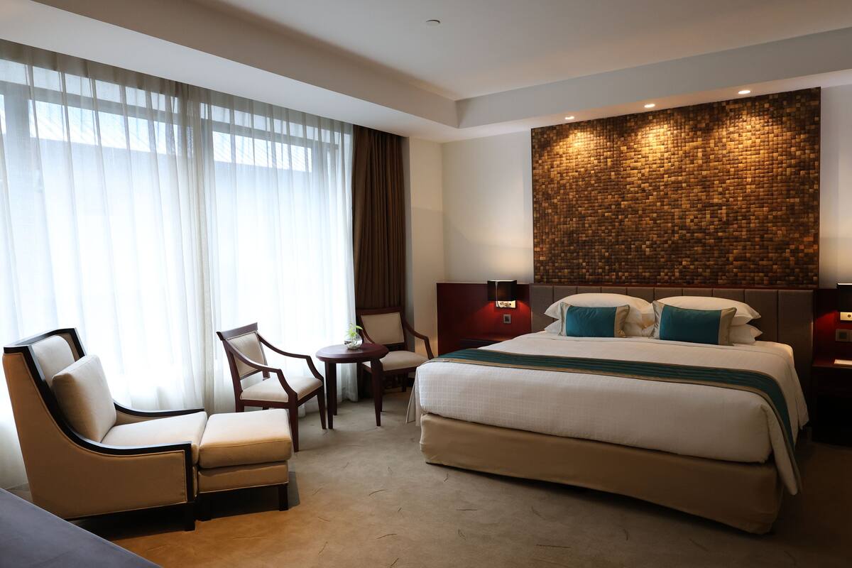 A hotel room with a large bed, two armchairs, a small table, and a wall-mounted TV.