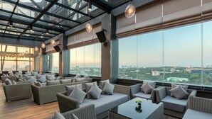 A modern lounge area with wicker furniture, large windows, and a city view. - Yangon Thanlwin Hotel (Yangon)
