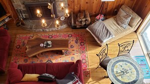 Ein gemütliches Wohnzimmer mit einem roten Sofa, einem beigen Sofa, einem Holztisch und einem Kamin mit brennenden Kerzen.
