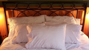 Ein ordentlich bezogenes Bett mit gesteppter Bettdecke und Kissen, ein Holz-Kopfteil und eine Nachttischlampe.