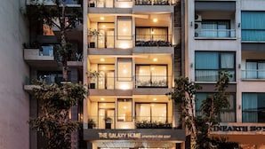A multi-story hotel with balconies, a staircase leading to the entrance, and potted plants.