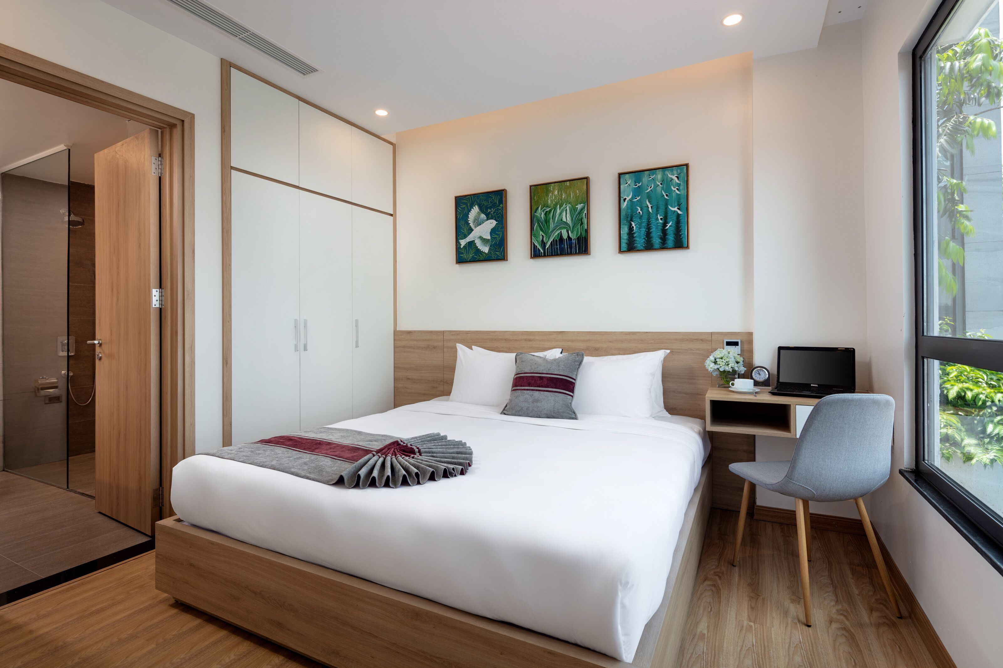 Une chambre d’hôtel moderne avec un grand lit, un bureau avec un ordinateur portable et des œuvres d’art accrochées au mur.