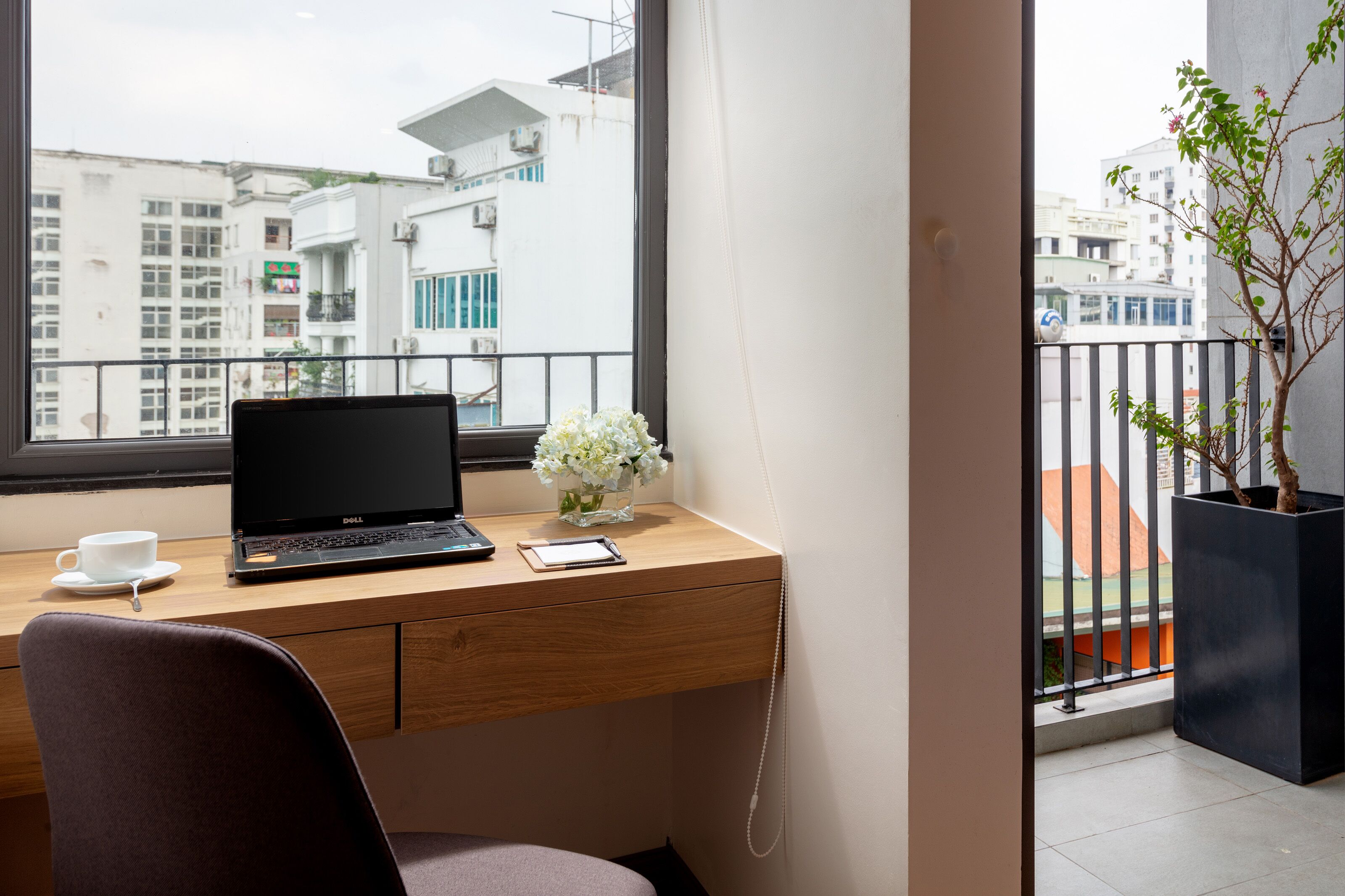 A modern office space with a wooden desk, a laptop, a cup, and a vase of flowers.