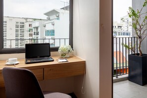 A modern office space with a wooden desk, a laptop, a cup, and a vase of flowers. - The Galaxy Home Hotel & Apartment (Hanoi)