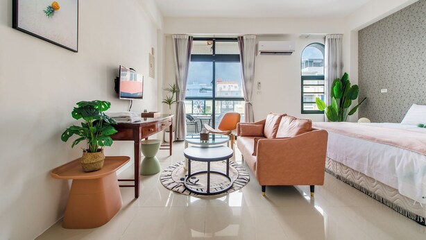A modern hotel room with a bed, a sofa, a desk, and a dining table. There are potted plants and a view of buildings outside the window. - Sakura B&B (Taitung)
