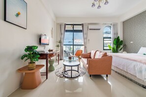 A modern hotel room with a bed, a sofa, a desk, and a dining table. There are potted plants and a view of buildings outside the window. - Sakura B&B (Taitung)