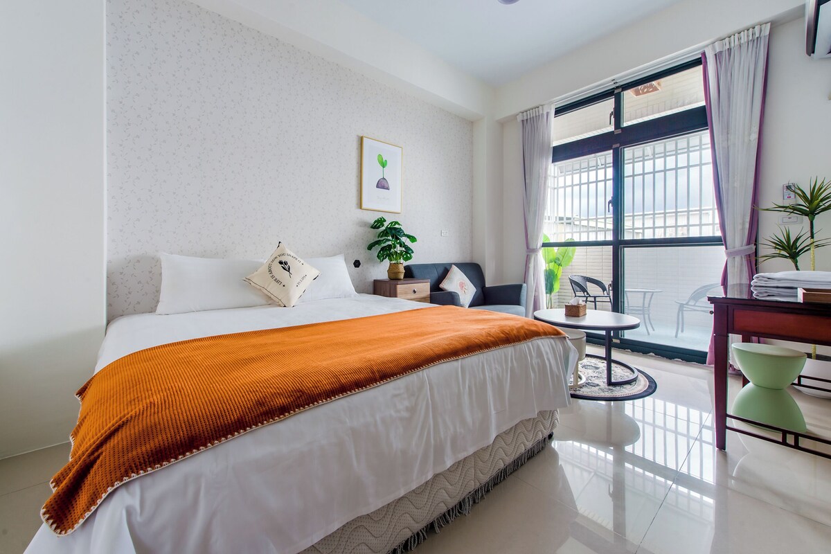 A hotel room with a bed, a small round table, a chair, a desk with a chair, and a window with curtains.