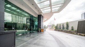 A modern building with a glass facade, a stone wall with greenery, and a clear sky. - OYO Home 89311 Marvelous 1br Starview (Gelang Patah)