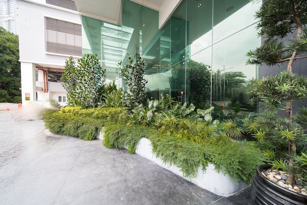 A modern building with large glass windows and a landscaped area with various plants and a small tree.
