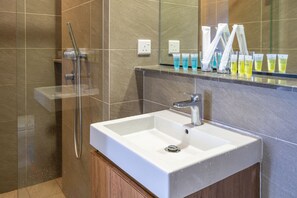 A bathroom with a white sink, a glass shower enclosure, and toiletries on the counter.