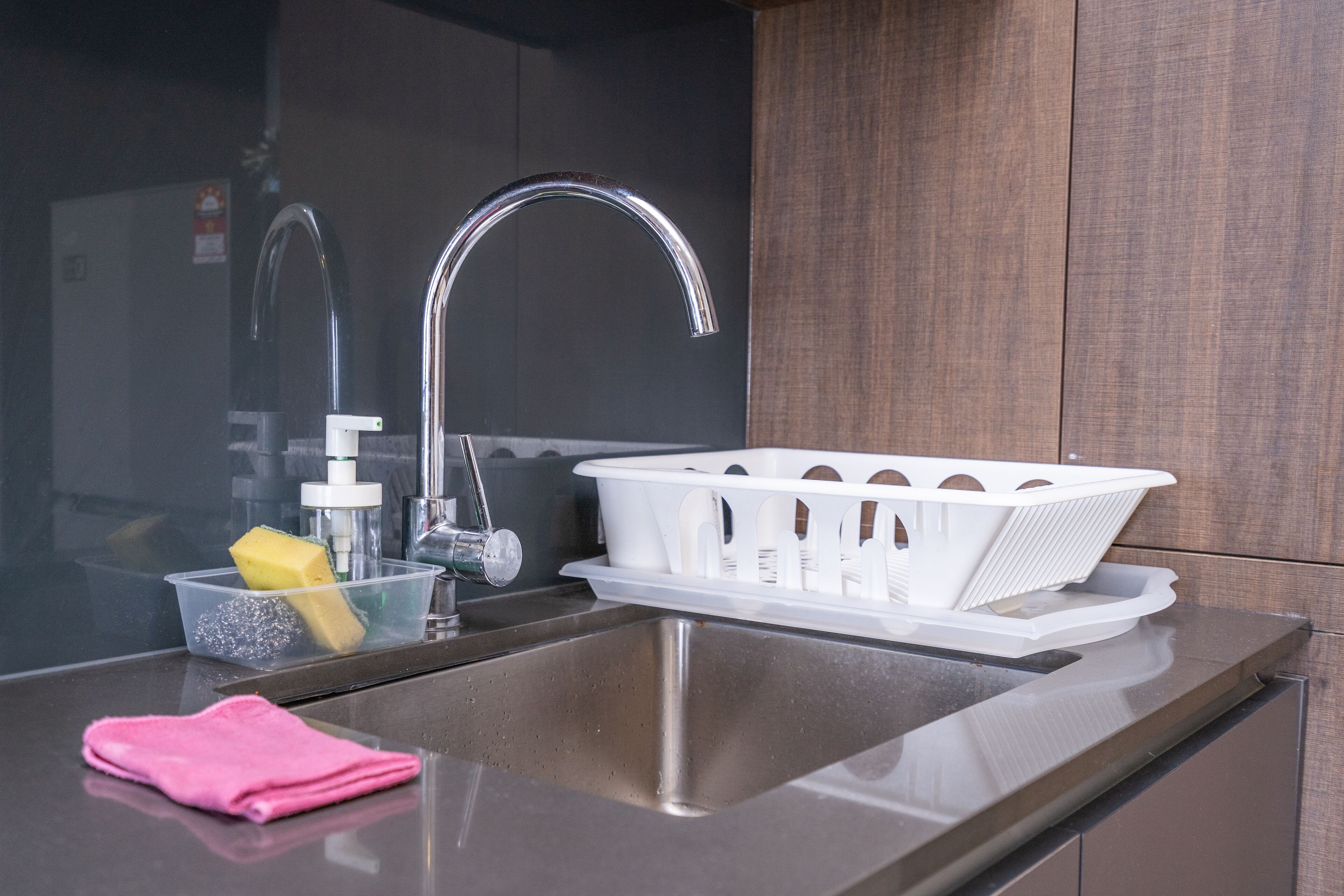 A modern kitchen with a stainless steel sink, a white plastic basket, and a pink towel on the counter.