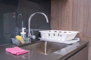 A modern kitchen with a stainless steel sink, a white plastic basket, and a pink towel on the counter.