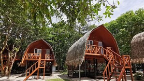 Zwei strohgedeckte Bungalows mit Holzbalkonen und Treppen, umgeben von dichtem Grün.