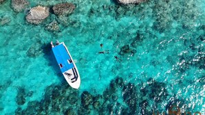 Eine Vogelperspektive auf ein Boot auf klarem türkisblauem Wasser, mit sichtbaren Felsen.
