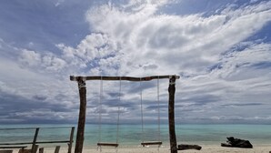 Ein hölzerner Schaukelstuhl am Strand mit Blick auf das Meer und einem bewölkten Himmel.