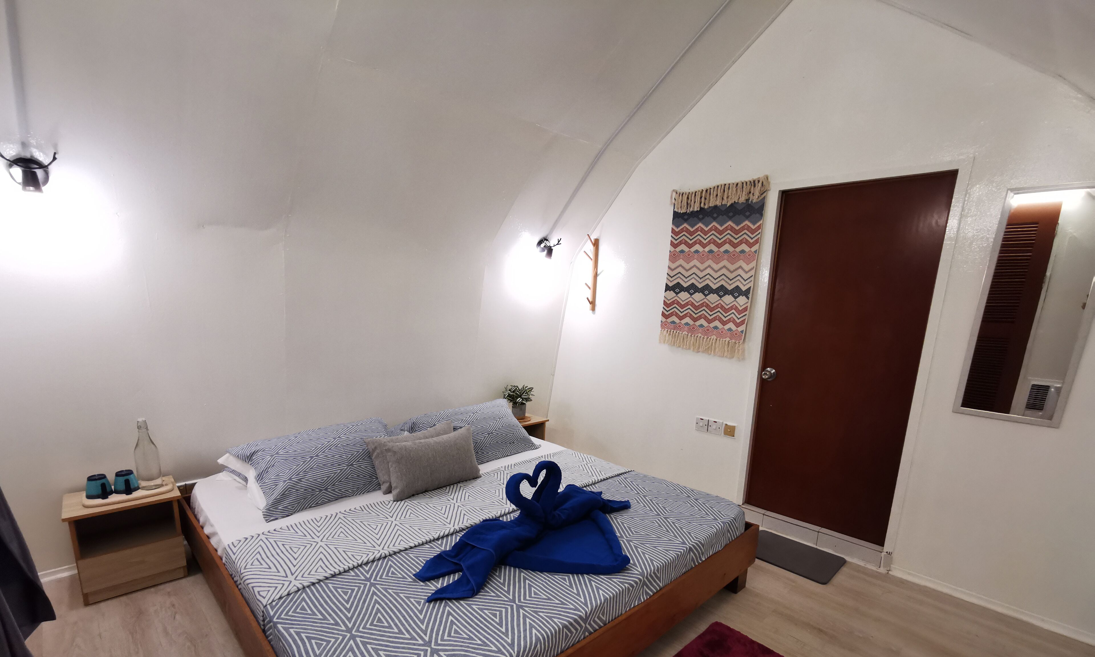 A bedroom with a bed, bedside tables, a wall-mounted heater, a door, and a window.