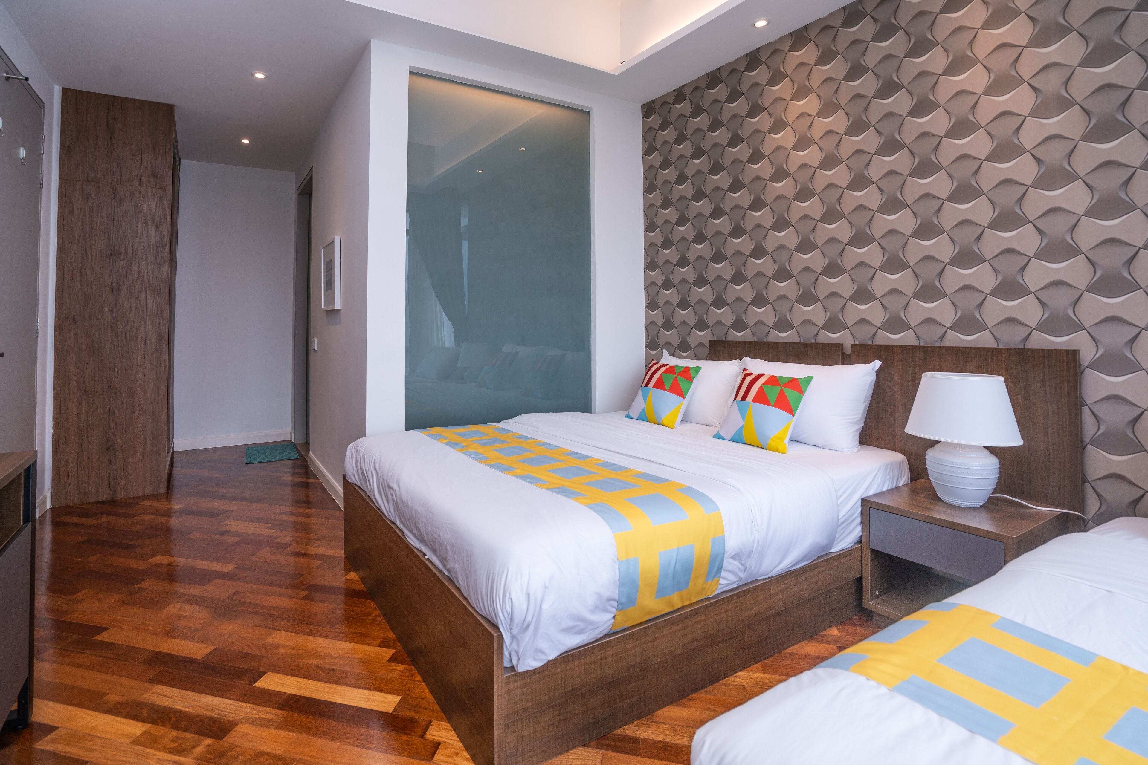 A modern hotel room with a large bed, a bedside table with a lamp, and a patterned wall.