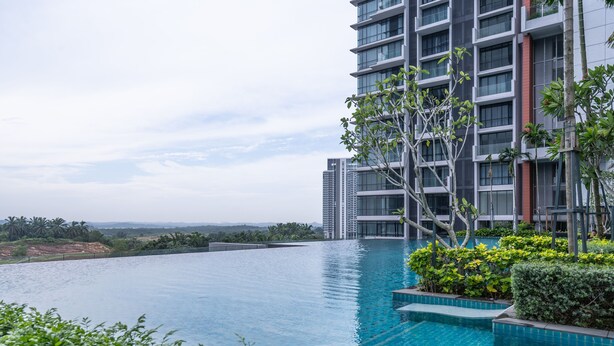 Un hôtel moderne doté d’une grande piscine à débordement, entouré d’une végétation luxuriante et offrant une vue sur les bâtiments situés au loin.