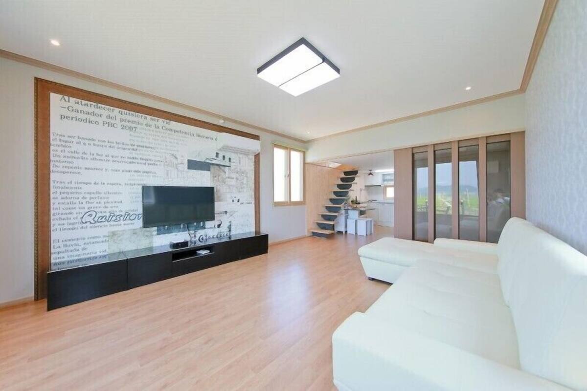 A modern living room with a white sofa, a flat-screen TV, and a large wall mural.