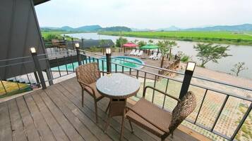 A wooden deck with a pool, wicker furniture, and a view of a lake and hills.