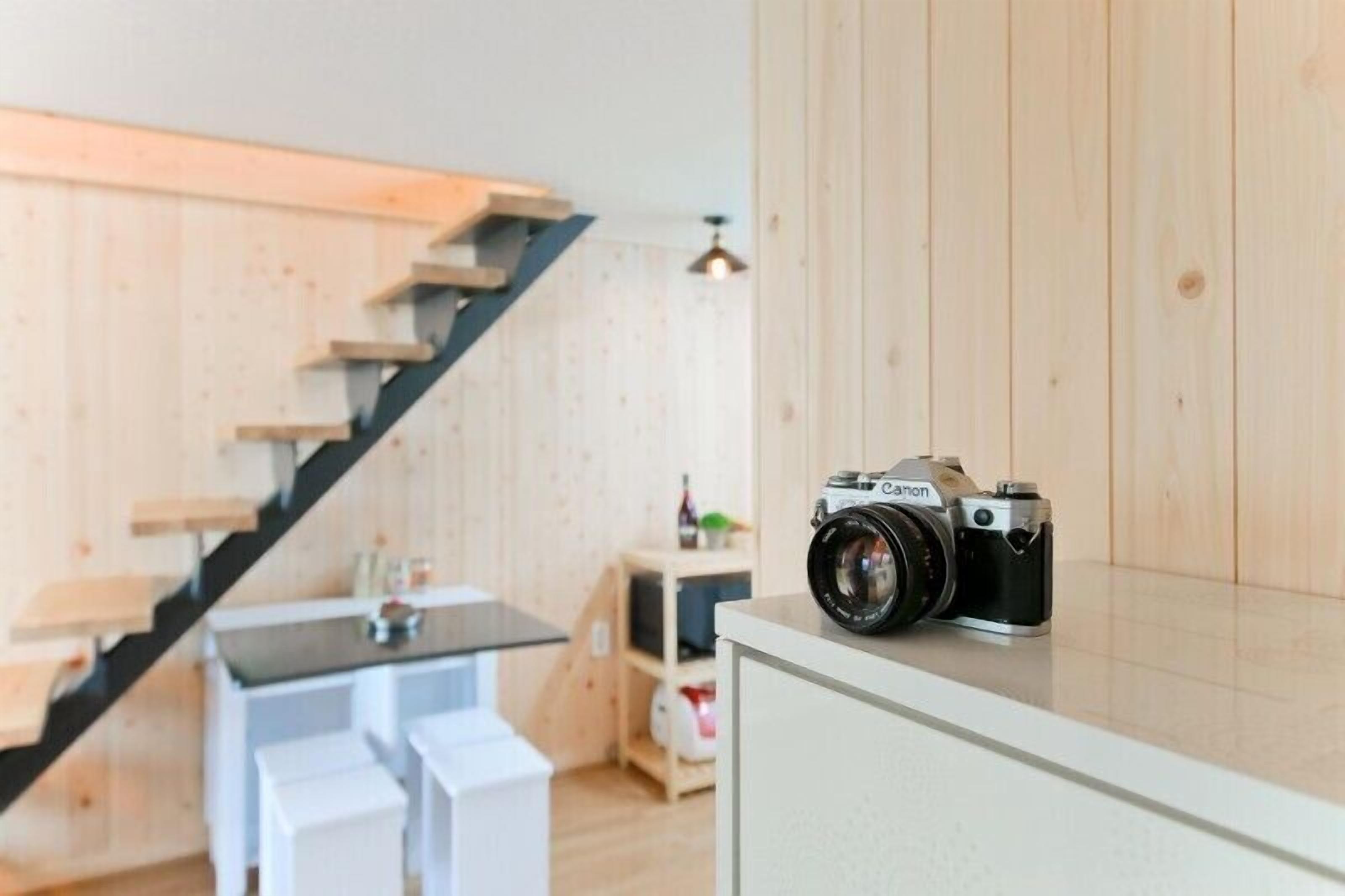 A modern interior with a wooden staircase, a dining area, and a camera on a counter.