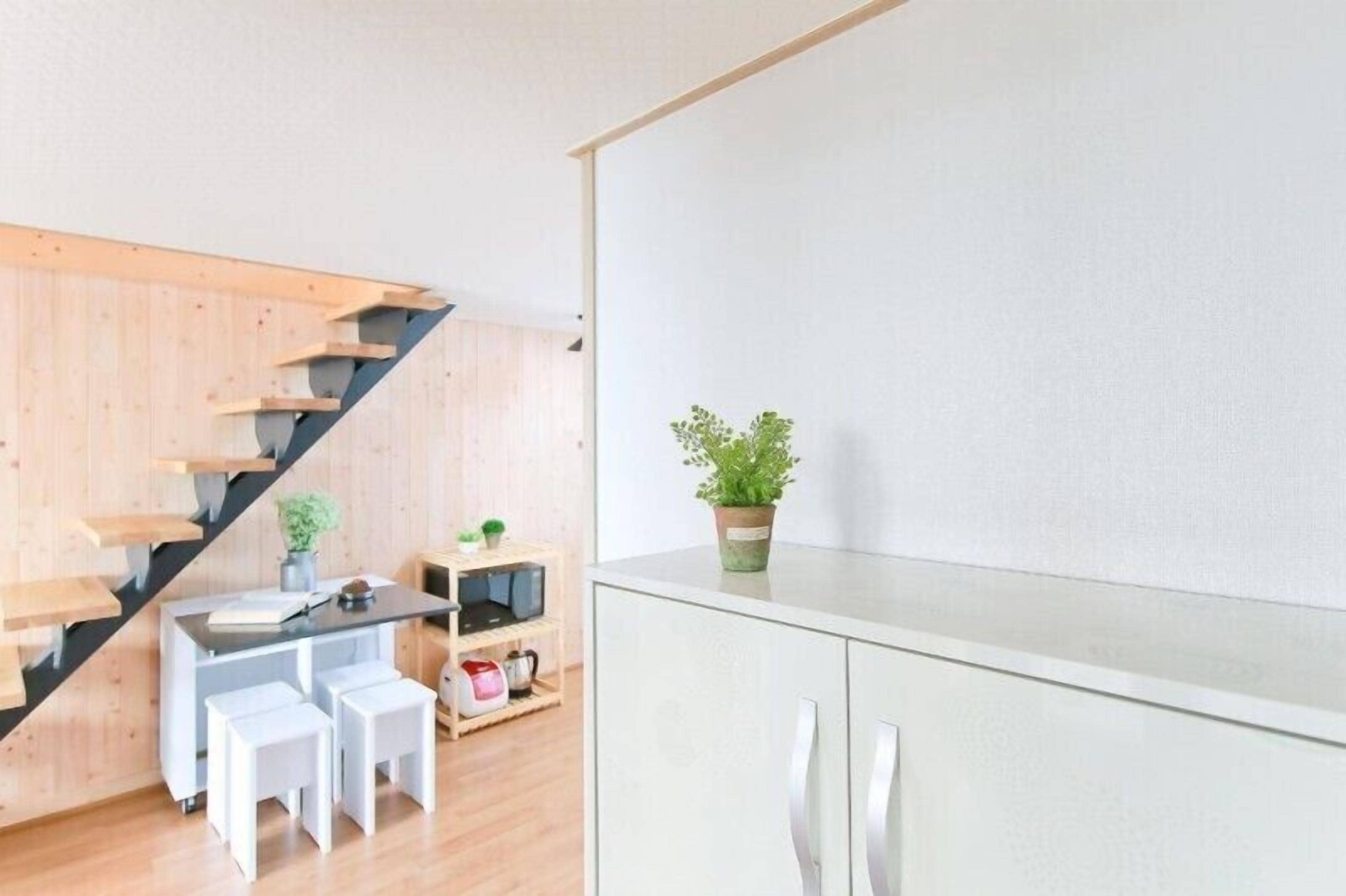Una cocina moderna con una escalera de madera, un comedor con taburetes blancos y una planta en maceta sobre la encimera.