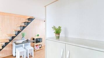 Una cocina moderna con una escalera de madera, un comedor con taburetes blancos y una planta en maceta sobre la encimera.