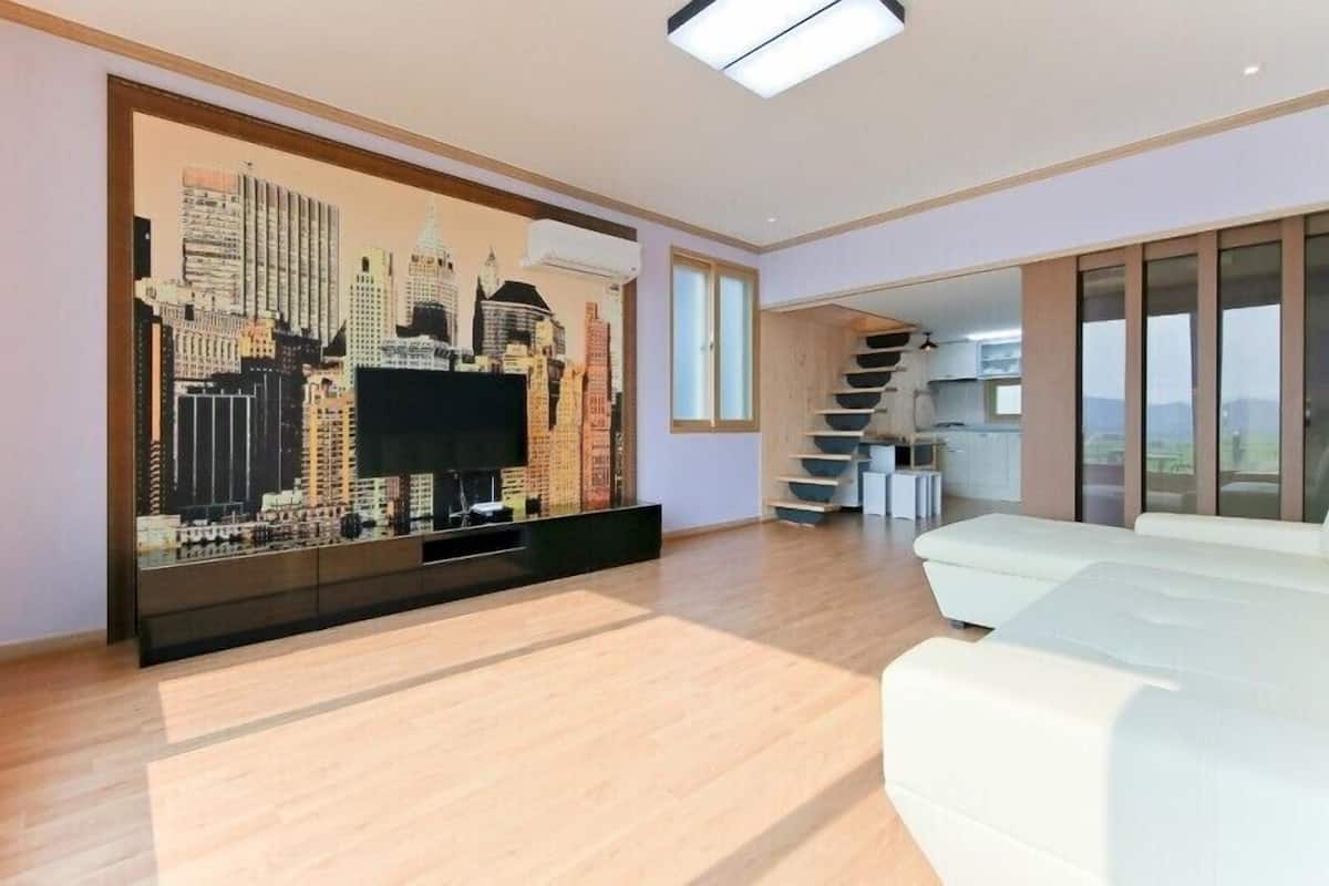 A modern living room with a cityscape mural, a flat-screen TV, a white sofa, and a staircase leading to an upper level.